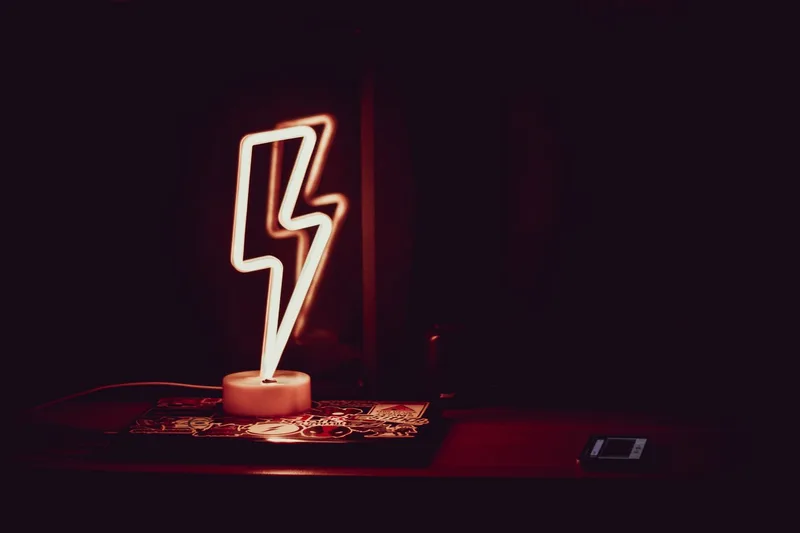 Modern neon night light in shape of lightning placed on table and reflected in mirror in dark room