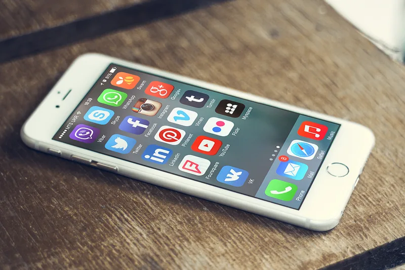 A smartphone resting on a wooden table with rows of social and messaging app icons on its screen